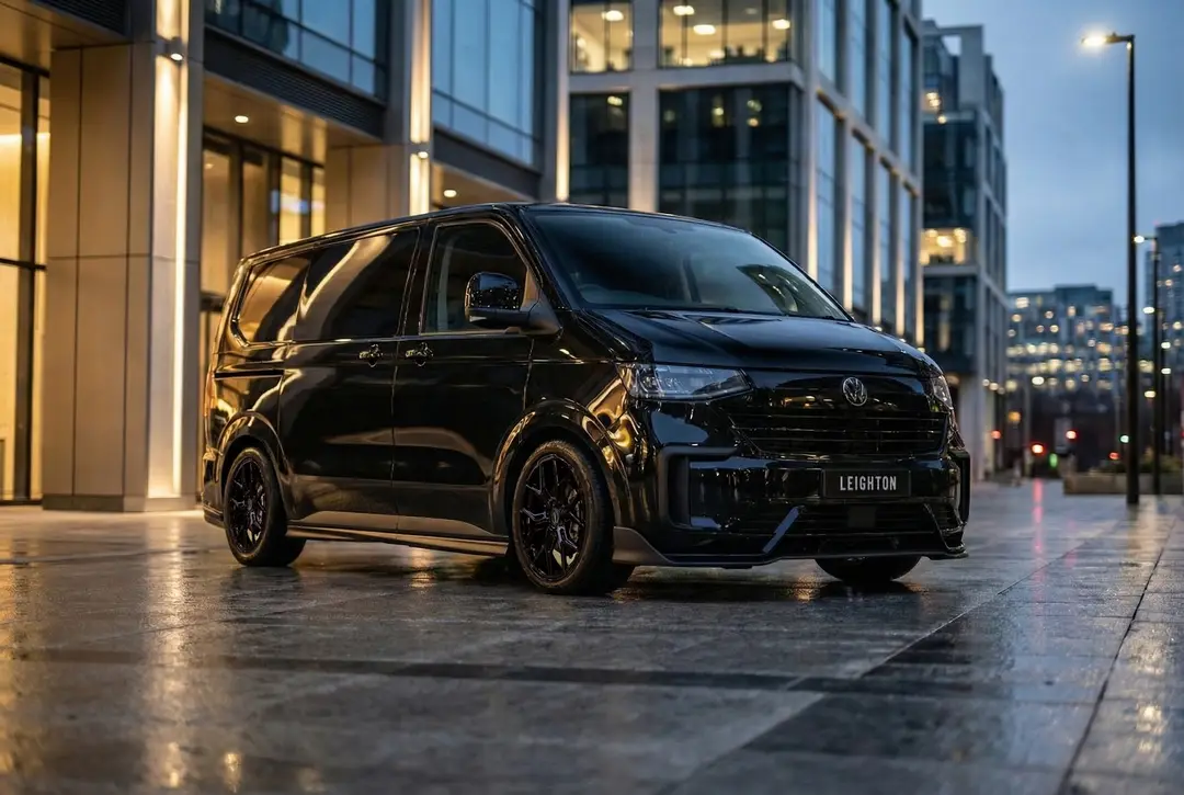 Black VW Transporter T7 outside a glass office building at dusk
