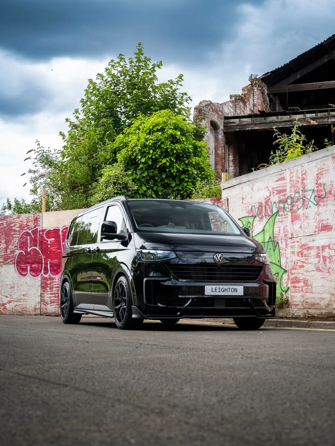 Black VW Transporter T7 kombi in front of a graffiti wall, low angle